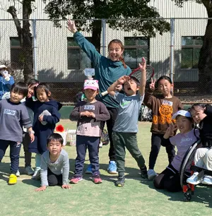 テニスコートで楽しそうに手を上げる子どもたちとコーチ